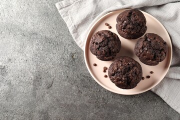 Delicious chocolate muffins on grey textured table, top view. Space for text