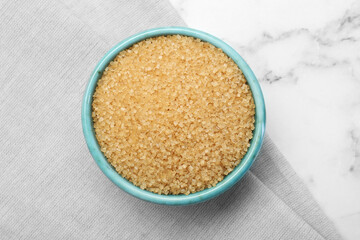 Brown sugar in bowl on white marble table, top view