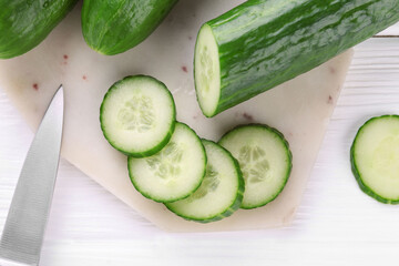 Cucumbers, knife and marble cutting board on white wooden table, top view