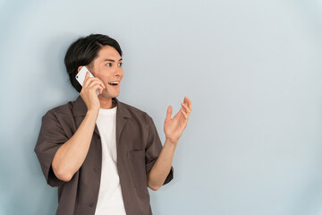 驚いた表情で電話する若い男性（びっくり・驚く・サプライズ・驚愕）
