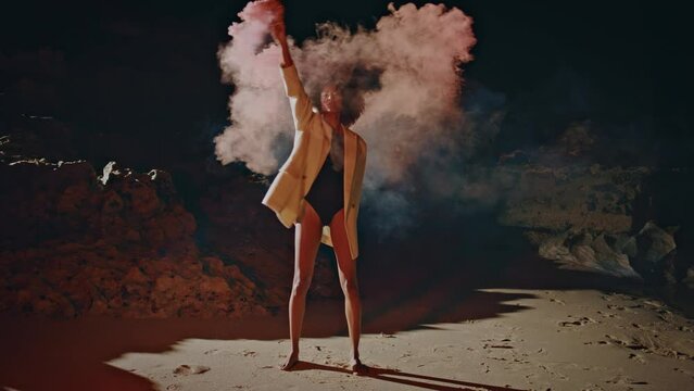 Party girl holding smoke grenade at night beach. Creative woman waving bomb
