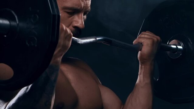 Fit and sporty bodybuilder over black background. Bodybuilder training using barbell. The concept of sport and fitness.