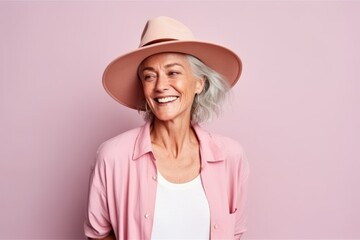 Portrait of a smiling senior woman wearing hat on pink background.