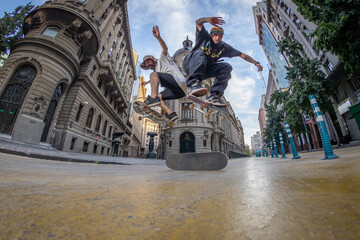 Two friend skaters jumping over a skateboard in downtown Santiago on a sunny day during summer shot...