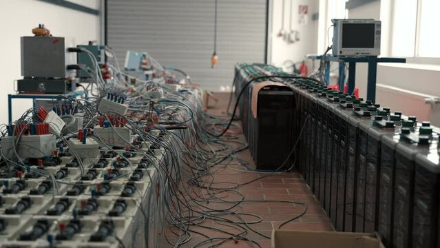 A look into a storage hall with planty of lead-acid traktion batteries with a lot of cables looking chaotic ready for controland tests