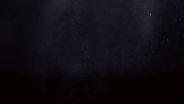 Misty spray water droplets shimmer in soft light as they fade against black background
