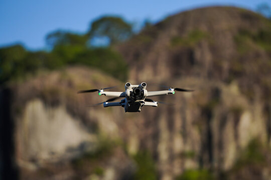 A small sized drone flying with rocky mountain backgrounds. Mini remote control aircraft on flight in outdoor area. Concept for travel ultralight drone.