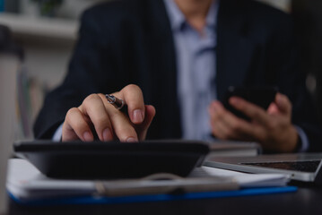  businessman hands using a smartphone and calculator simultaneously, reflecting multitasking and...