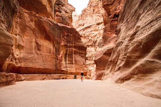 Caucasian tourist woman walk at Petra entrance al-siq tunnels surrounded by huge canyon rock formations