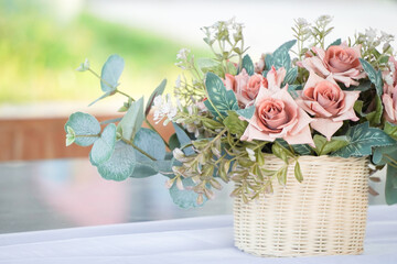 Modern interior design of modern dining room or office workplace with artificial plant. Plastic rose flower bouquet with woven rattan pots on the table with empty blank copy text place.