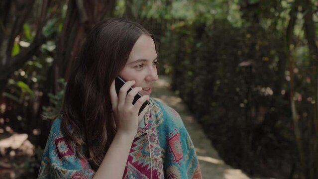 a girl in colorful clothes speaks on the phone against the backdrop of a tropical forest