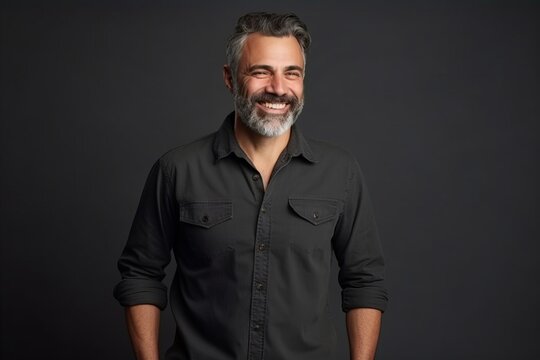 Portrait of a handsome mature man with grey hair and beard smiling at the camera against a dark background