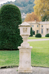 Fototapeta na wymiar Marble flowerpot with lid in the green garden of an ancient villa