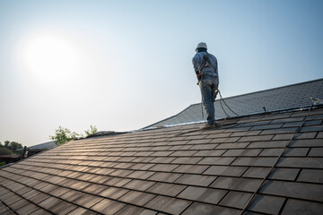 A Roof Repairman, Repair and Replace the House Roof with Handyman with Tools and Pprotective equipment. Stand on the Roof with the Ssky Background.