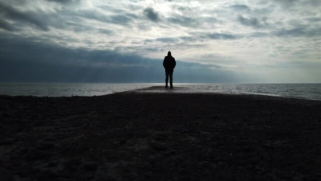 Man in a black coat walking on a concrete jetty to the infinite horizon of Lake Ontario
