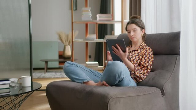 Young woman relaxes and uses tablet in modern living room, full shot
