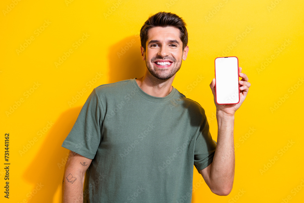 Poster portrait of satisfied smart guy wear stylish t-shirt demonstrate smartphone screen menu empty space 