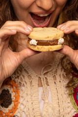 Young female eating a tasty Argentinean alfajor with dulce de leche. Close up, vertical.