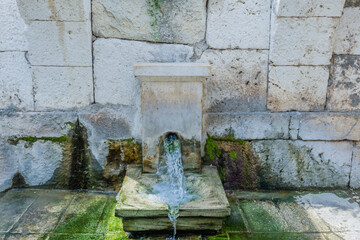 Water flows from an ancient stone fountain with green algae on the base in Izmir, Turkiye.