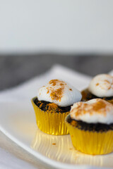 Chocolate cupcakes with white marshmallow icing, real edible gold leaf sprinkles in a gold cupcake wrapper on a white plate with room for text in the image - 3 cupcakes portrait