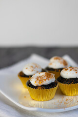 Chocolate cupcakes with white marshmallow icing, real edible gold leaf sprinkles in a gold cupcake wrapper on a white plate with room for text in the image - 4 cupcakes portrait