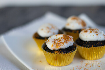 Chocolate cupcakes with white marshmallow icing, real edible gold leaf sprinkles in a gold cupcake wrapper on a white plate with room for text in the image - 4 cupcakes wide