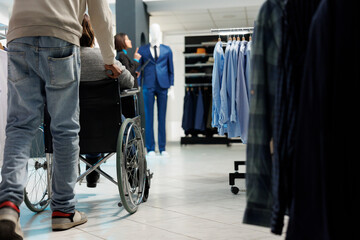 African american woman in wheelchair getting help while shopping for apparel in clothing store....