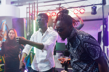 Carefree african american man drinking alcohol and dancing with friends in nightclub. Clubber...