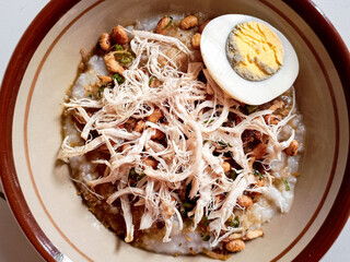 Bubur ayam or chicken congee is Chinese Indonesian rice porridge topped with shredded chicken and various savoury condiments served on bowl and isolated on white background.
