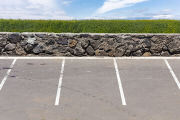 Parking vide avec muret et haie vive en arrière plan 