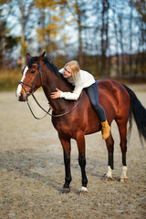Obraz premium Young blonde girl with her brown horse on the riding arena in portraits.