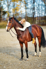 Obraz premium Young blonde girl with her brown horse on the riding arena in portraits.