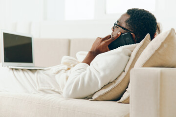 Smiling African American Man Working on Laptop in Home Office, Talking on Phone, Surrounded by Modern Technology and Comfort