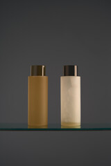 Two clear plastic cosmetic bottles with lids on glass stand. Shower gel, shampoo. Mockup, brand packaging, studio product photo. Minimalist luxury design. Gray backdrop, copyspace