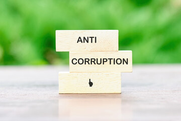 Anti corruption phrase written on wooden blocks against a background of green plants out of focus