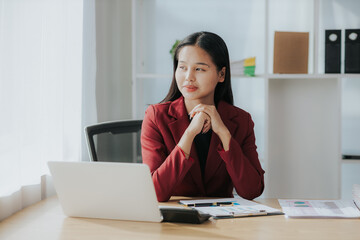 Cute Asian businesswoman in suit in modern workplace. Thai woman. Southeast Asian woman. looking at laptop in office