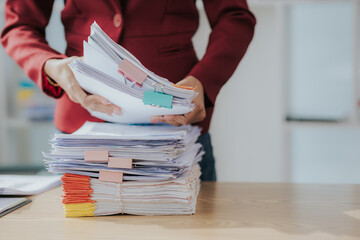 Woman's hands working in stacks of paper files to find and check unfinished documents, success in...