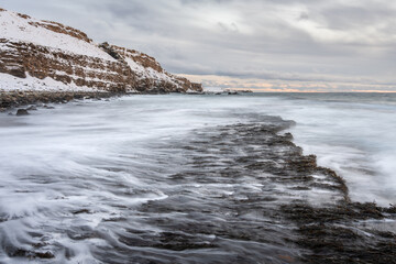 Water flowing over the rock on the shore of the Varangerfjorden on a cold winter day during the polar night, Northern Norway