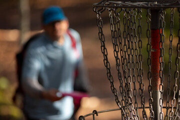 Medium shot of the chains on the basket with an out-of-focus disc golfer preparing to putt in the...