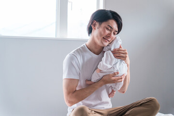 寝室で赤ちゃん・新生児と過ごす若い男性（育児休業・イクメン）
