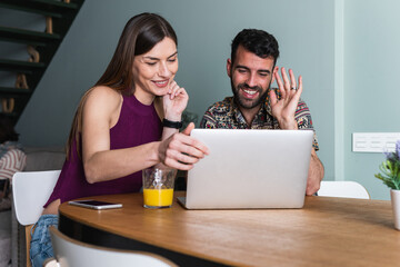 Young couple, video call and laptop to connect, have conversation and online chatting with juice in living room. Digital device, man and woman happy for communication or wave at screen