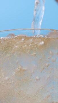 4K footage vertical video Front view SLO MO CU, Pouring soda mixed with alcohol into the glass of ice with splashes on a blue background