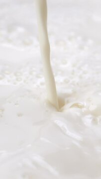 4K footage vertical video Front view SLO MO CU, Pouring fresh milk and Splashing.