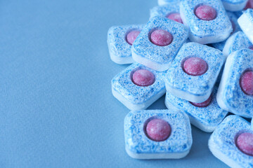 Dishwasher tablets on blue background, selective focus. Copy space.