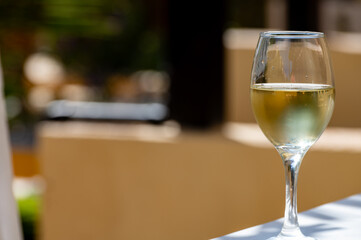 Glass of cold white wine on white terrace table outdoor in sunny day