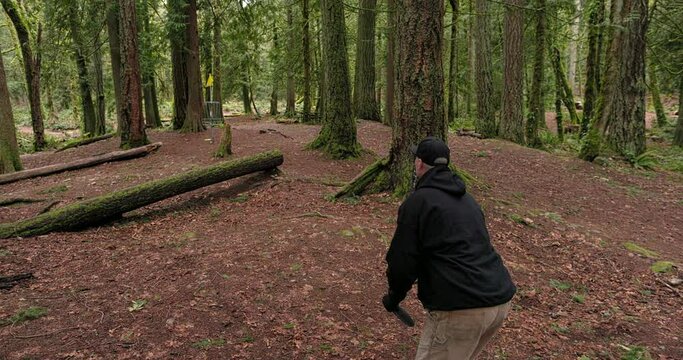 Wide shot of a man sinking a long putt while playing disc golf on the Kitsap Peninsula in the Pacific Northwest in slow motion at 120 fps