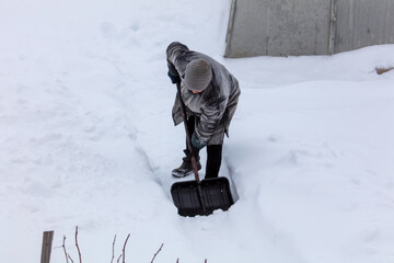 A woman cleans snow with a shovel near a greenhouse