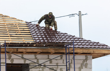 Workers install tiles on the roof of a house in winter