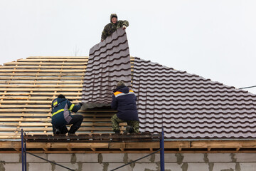 Workers install tiles on the roof of a house in winter