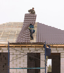 Workers install tiles on the roof of a house in winter